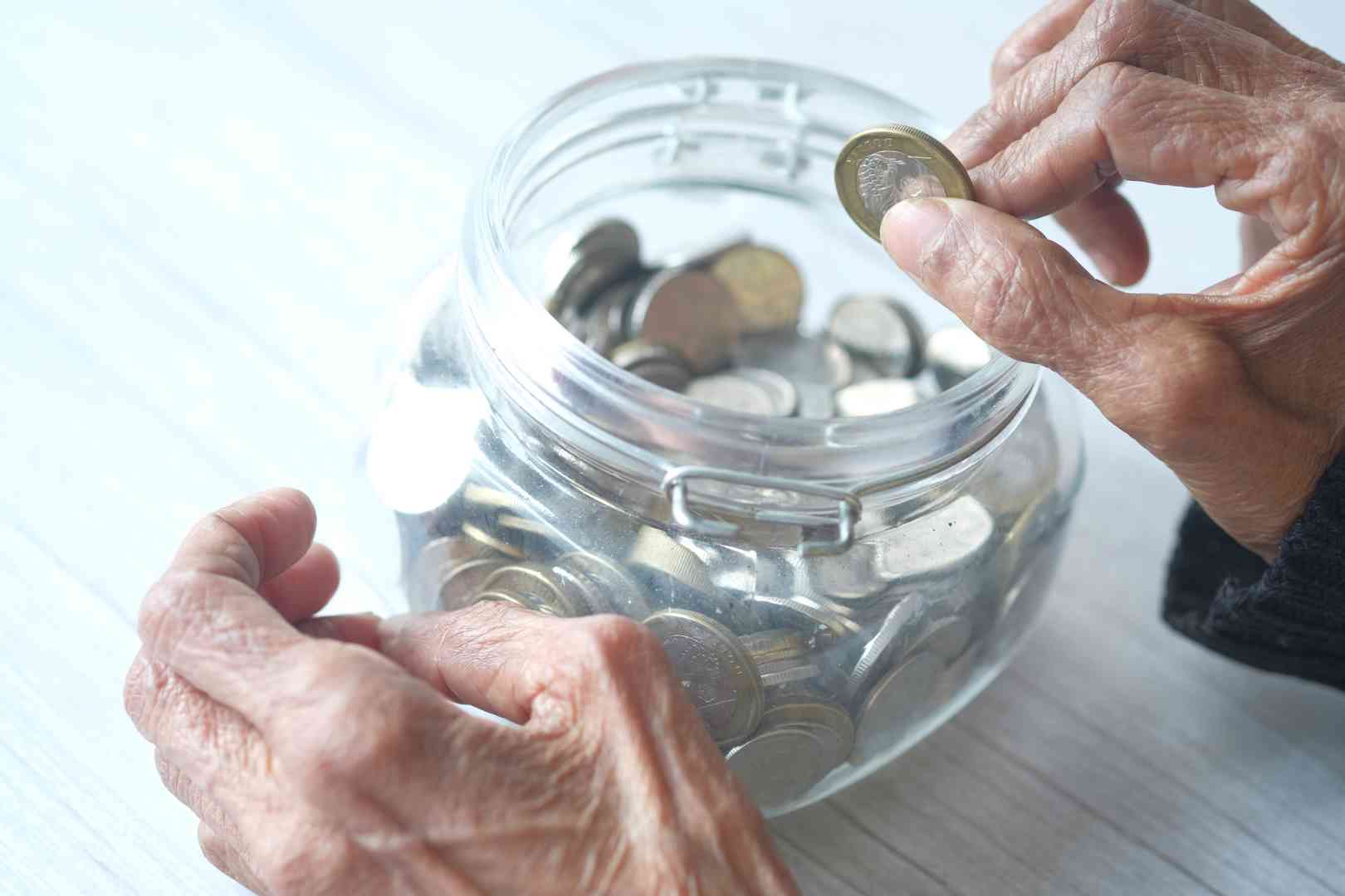 Close up of senior women hand saving coins in a jar
